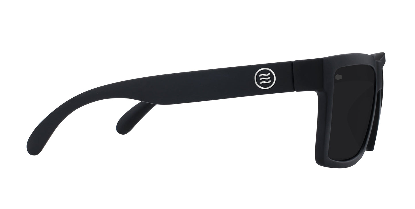 The Neven Eyewear Lowrider sunglasses are shown in side profile, featuring thick black frames, dark lenses, and a small white circular logo with wavy lines on the temple arm against a plain white background.