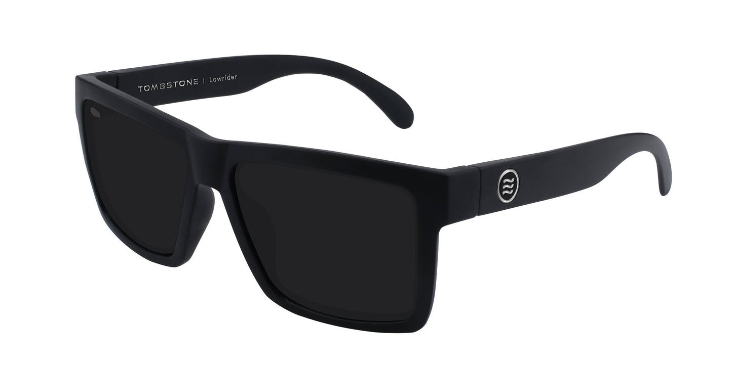 A pair of matte black rectangular Neven Eyewear Lowrider sunglasses with dark lenses and a thick, angular frame, featuring a round silver logo and LOWRIDER printed inside the arm. Shown on a plain white background.