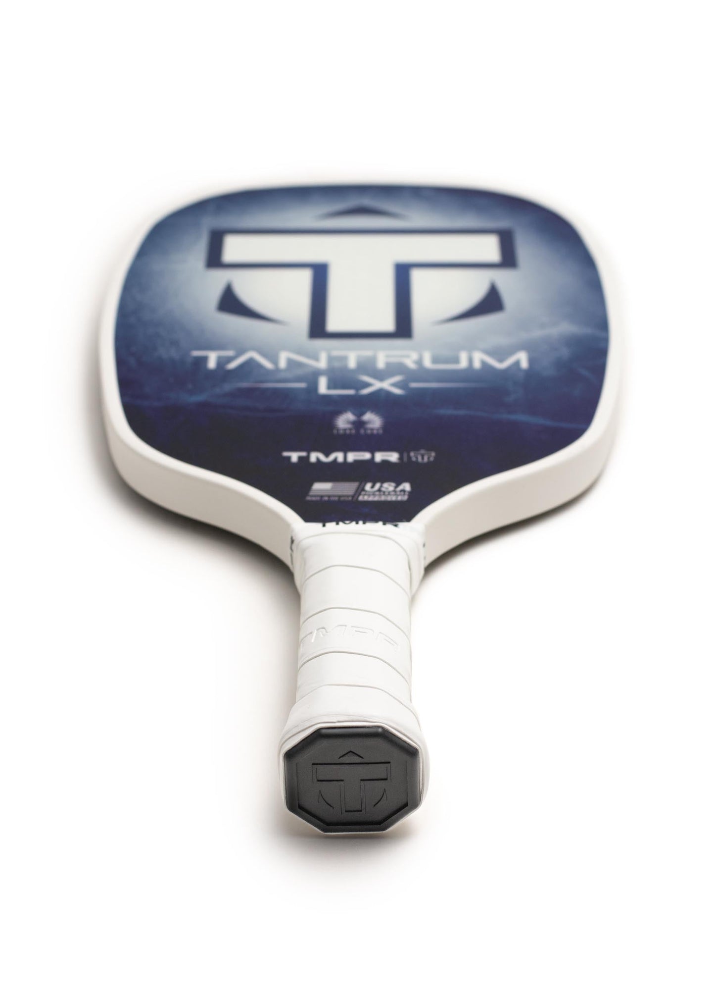 A close-up of the TMPR Sports Tantrum LX | Indigo Ice pickleball paddle lying flat, handle forward, highlights its bold blue and white design, honeycomb polymer core for performance, and vibration dampening technology.