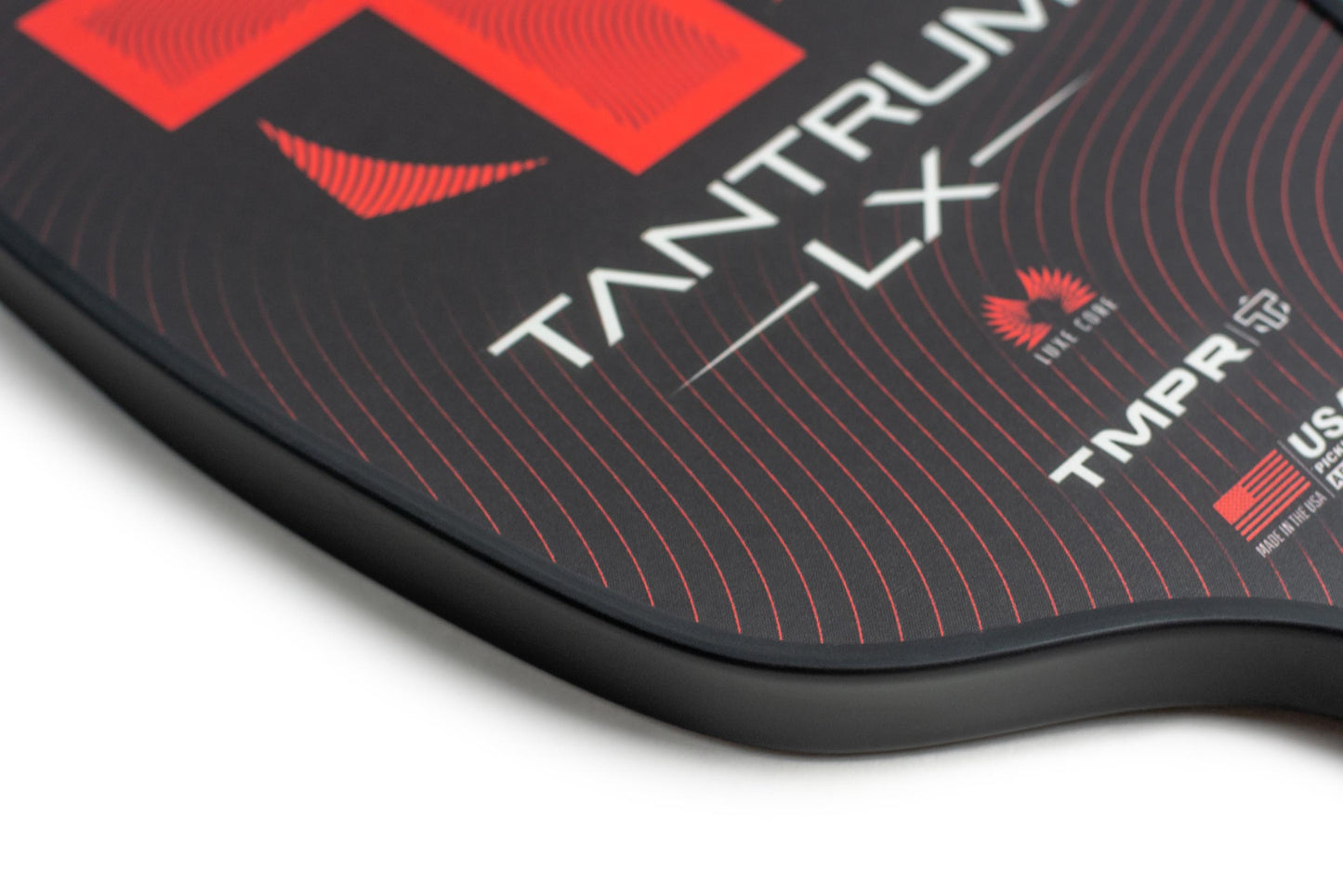 Close-up of the TMPR Sports Tantrum LX pickleball paddle, featuring a black, longer face with red wavy lines, “TANTRUM LX” in white, and logos for TMPR Sports, USAPA Approved, plus a red feather on its textured surface for better performance.