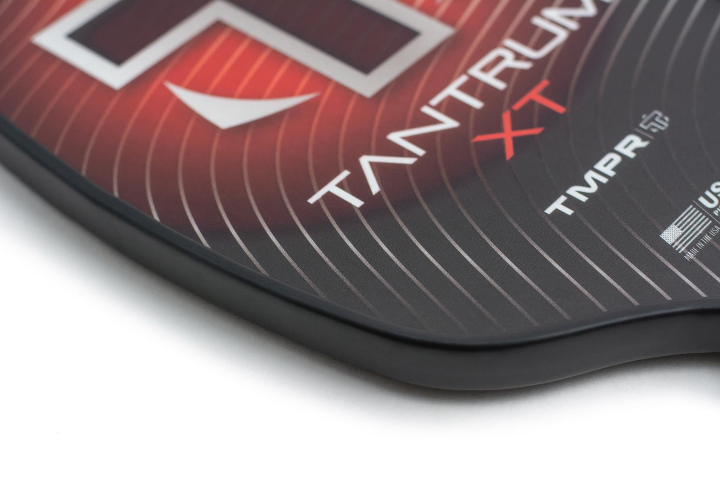 Close-up of the Tantrum XT pickleball paddle by TMPR Sports, showing its name on a black and red background with curved white lines, black edges, and part of the USAPA-approved logo. Features a honeycomb polymer power core.