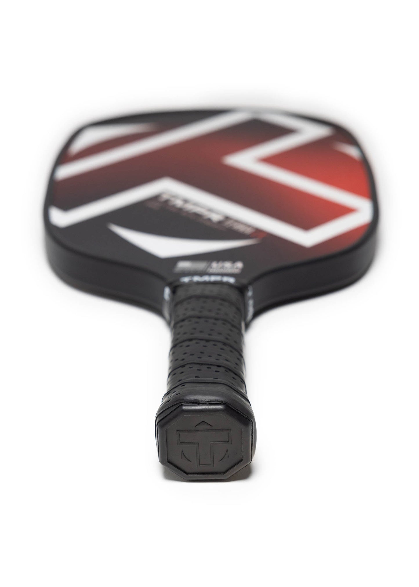 A close-up of the TMPR Sports Terra LX pickleball paddle, showing its textured grip and red, white, and black geometric design. The handle with vibration dampening tech is in sharp focus with a TT logo on the end cap.