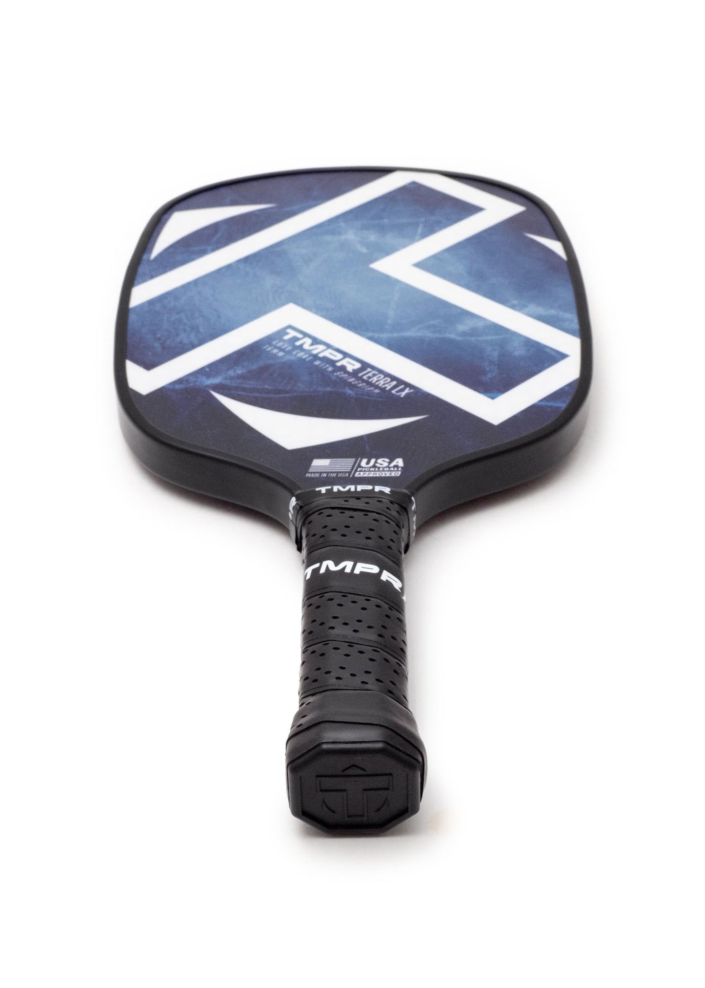 A close-up of the TMPR Sports Terra LX | Indigo Ice pickleball paddle, featuring a dark grip and a blue face with a bold white geometric pattern, lies face up on a white background.