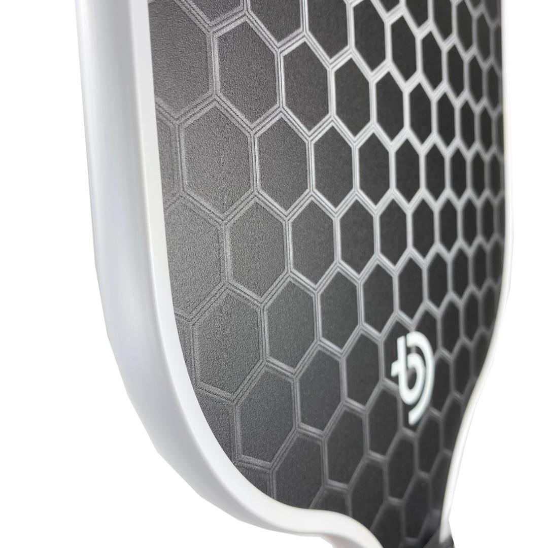 Close-up of The Big Dink Bundle by The Big Dink, a carbon fiber pickleball paddle with a black, raised hexagonal pattern and white edge guard—ideal for beginners wanting premium yet affordable performance.
