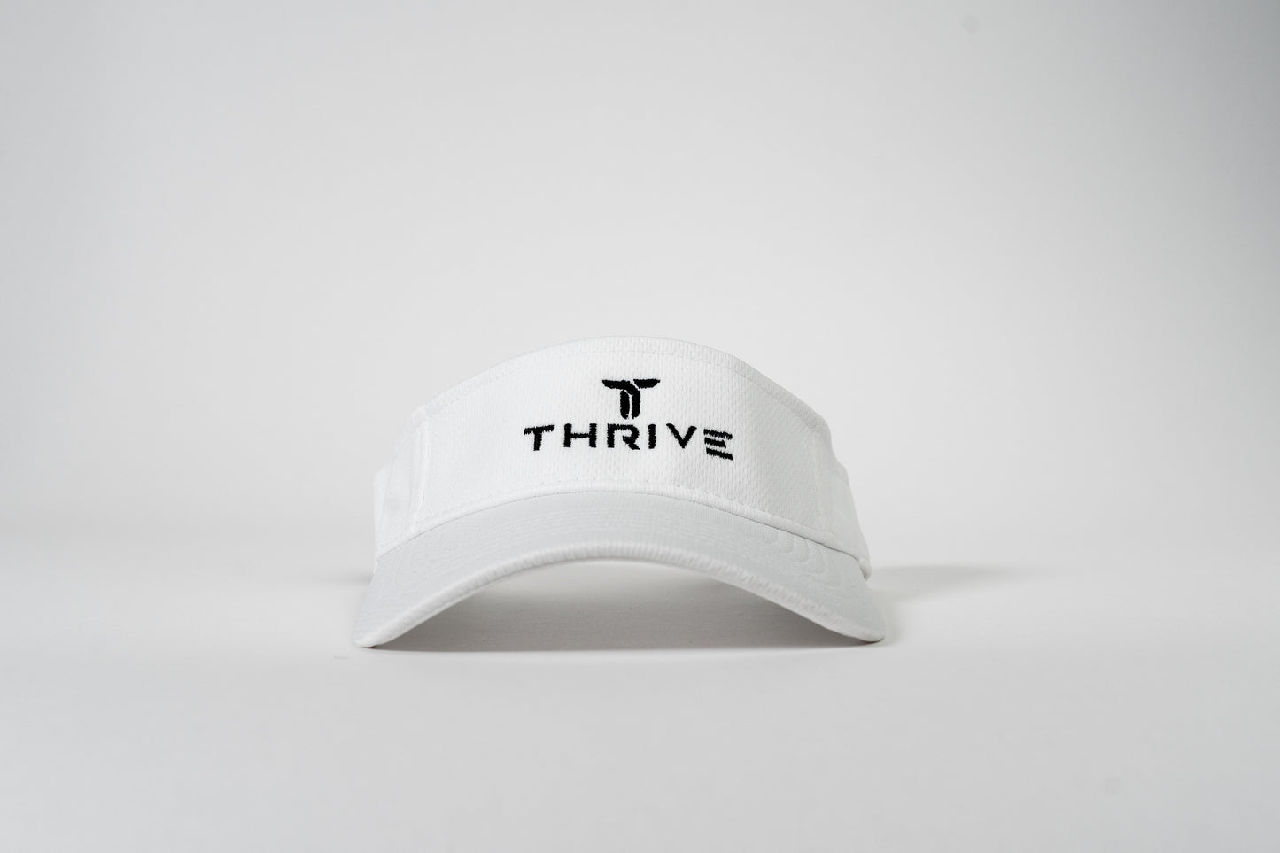 The Thrive Elite Tour Visor by Thrive Pickleball is a white, low-profile sports visor with "THRIVE" and a black logo embroidered above it. Featuring moisture-wicking textured fabric and a curved brim. Displayed on a plain white background.