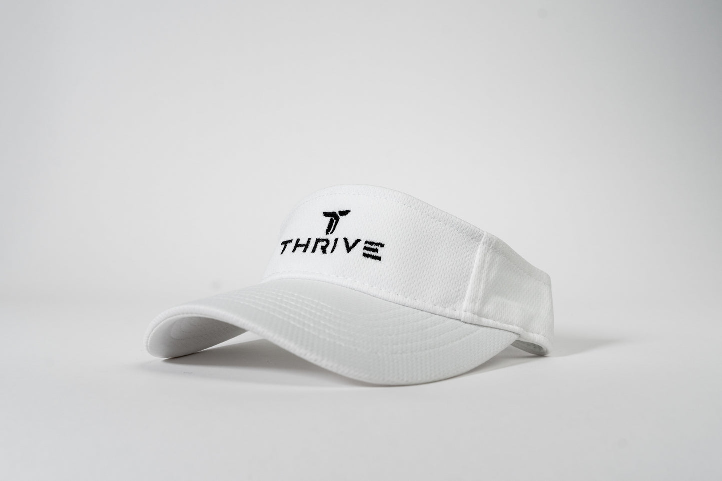 The Thrive Elite Tour Visor by Thrive Pickleball is a white, low-profile sports visor with a curved brim, featuring “THRIVE” and a black stylized T logo embroidered on the front, shown against a plain white background.
