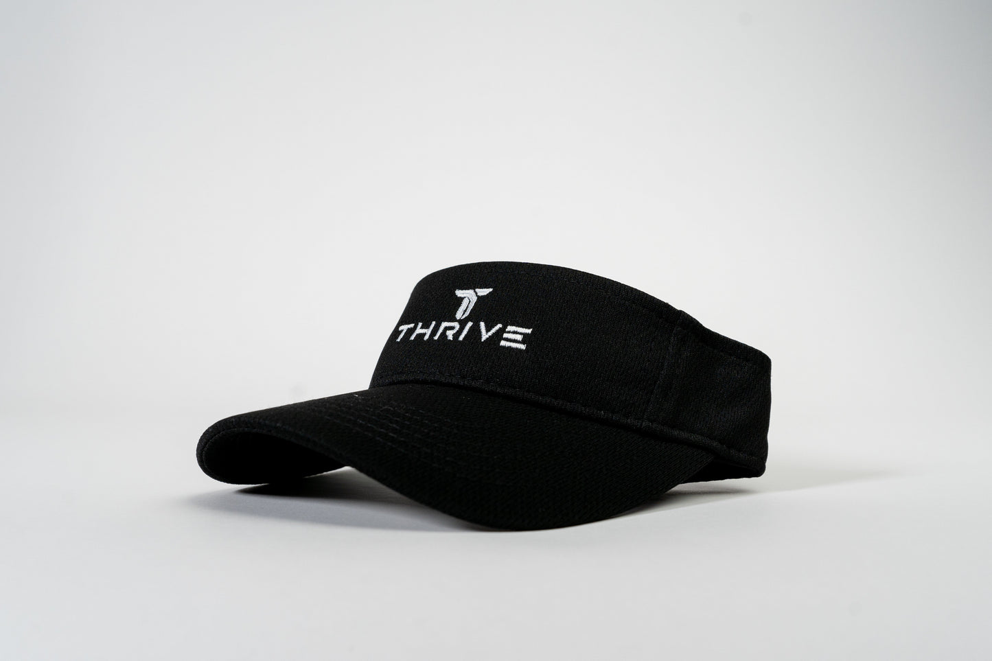 The Thrive Elite Tour Visor by Thrive Pickleball is a black, low-profile hat featuring "THRIVE" and a stylized T logo embroidered in white on the front band. The curved bill faces slightly left against a white background.