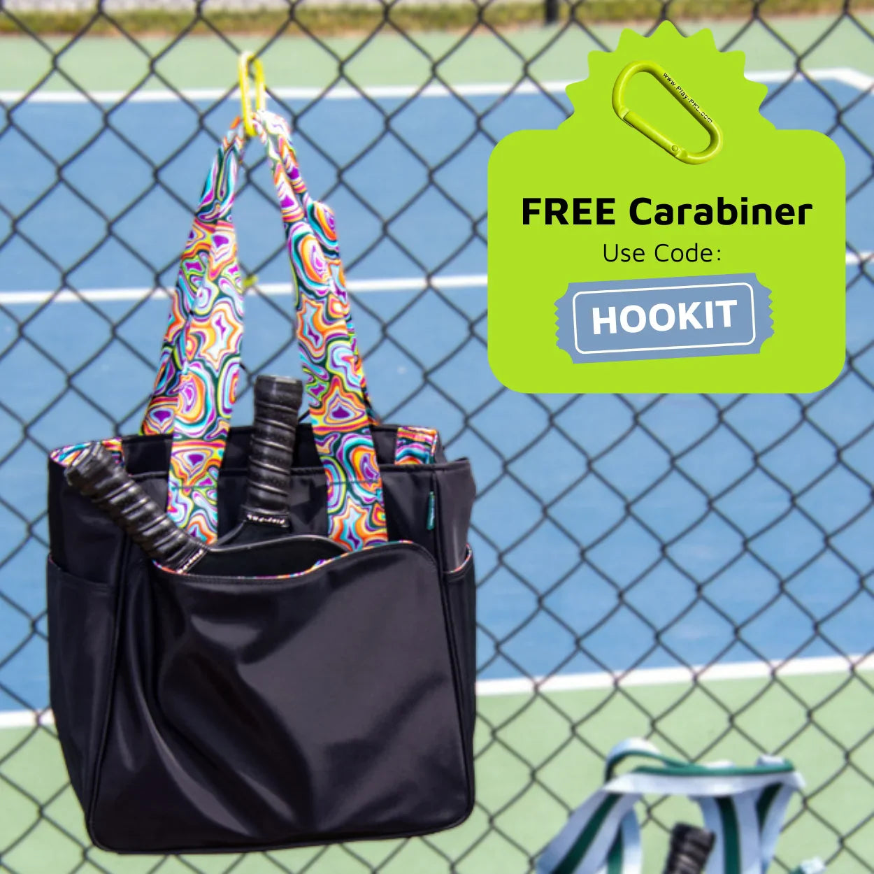 The Lulu Pickleball Tote from Playly Store, filled with rackets, hangs on a tennis court fence. A green graphic promotes a “FREE Carabiner” offer with code “HOOKIT,” showing an illustrated carabiner above the text.