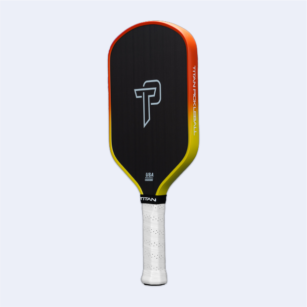 The Titan Pickleball Titan Ignite 16L paddle features black carbon fiber, a central white TP logo, orange-yellow gradient edges, TITAN PICKLEBALL on the right side, a textured white grip handle, and a plain light gray background.