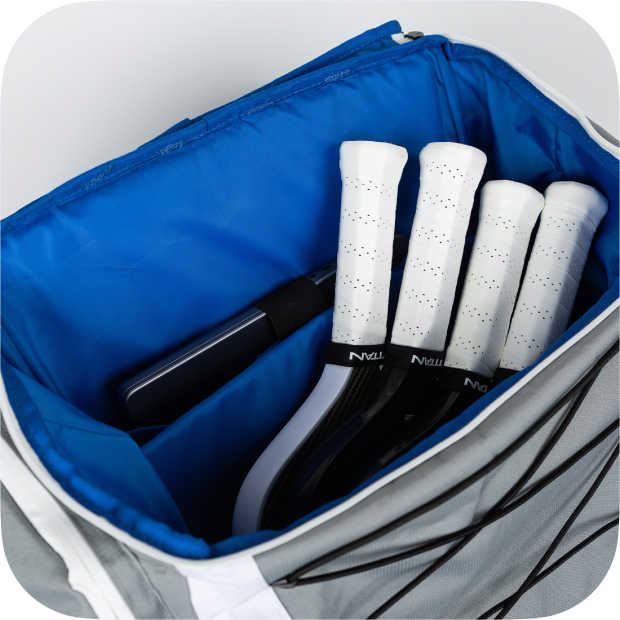 The Titan Pickleball Backpack by Titan Pickleball features a gray exterior and blue interior, storing four white-handled tennis racquets and a black cylindrical case neatly in separate compartments.
