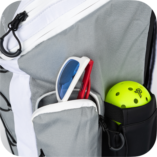 A close-up of the Titan Pickleball Backpack by Titan Pickleball shows its gray and white pocket holding red and white sunglasses, next to a black side pouch with a bright green pickleball featuring an “R” logo. The image has rounded corners.