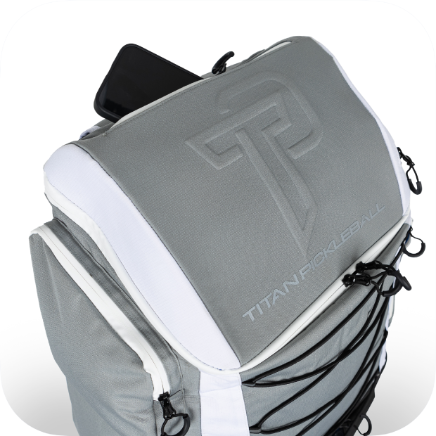 The Titan Pickleball Backpack by Titan Pickleball features a gray and white design with an embossed TP logo, front elastic cords, side zipper pulls, and an open top compartment displaying a black smartphone.