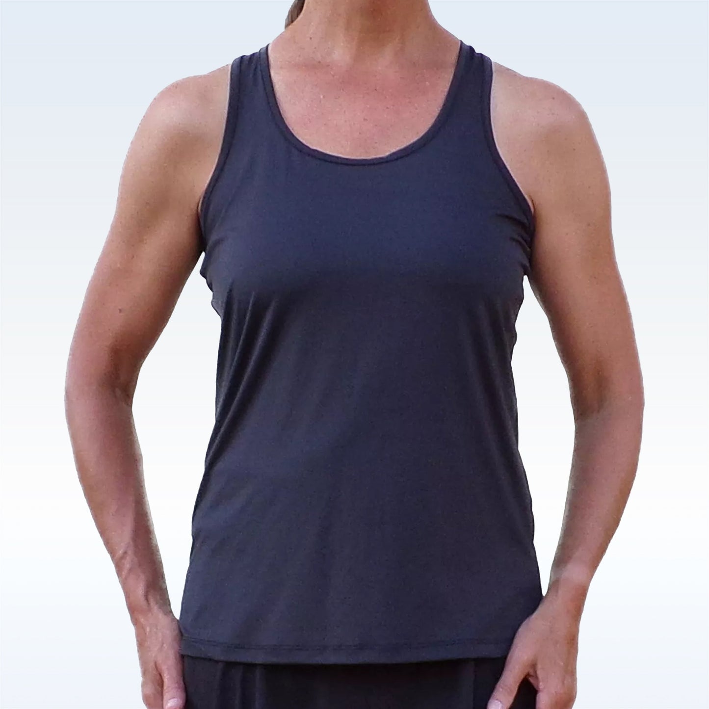 A woman faces forward against a light background, wearing the Pickleball Bella PB Racerback Tank Black with a racerback design and dark pants. Her hands are at her sides, and her face is not visible in the image.