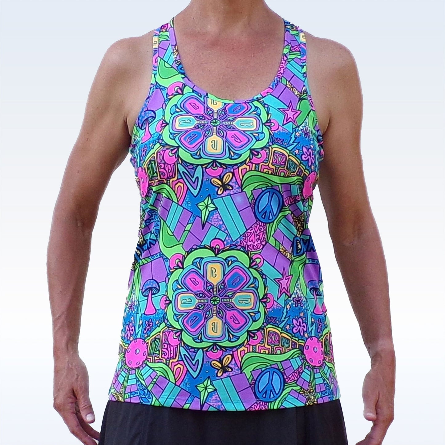 A person wears the Pickleball Bella PB Racerback Tank Groovy, featuring a vibrant psychedelic pattern with mandalas, peace signs, hearts, stars, flowers, and colorful abstract shapes on a light background.