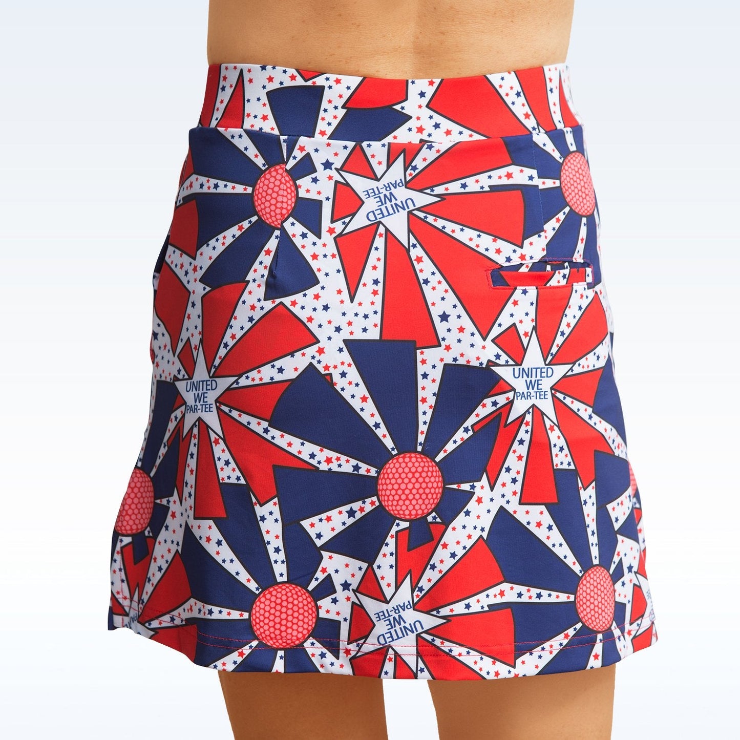 A person wears the Pickleball Bella United We Par-Tee Straight Golf Skort, showing only their lower torso and legs. The women’s skort features bold blue and red stars, starbursts, and "UNITED WE STAND" on a light background.