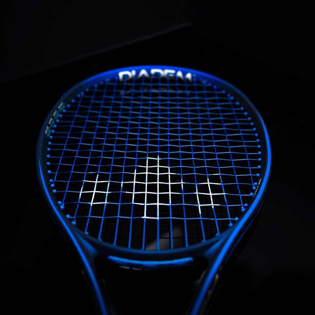A close-up of a blue tennis racket with dark blue strings on a glossy black surface, featuring the Diadem Sports logo—ideal for highlighting your Diadem Stencil and Ink Bundle.