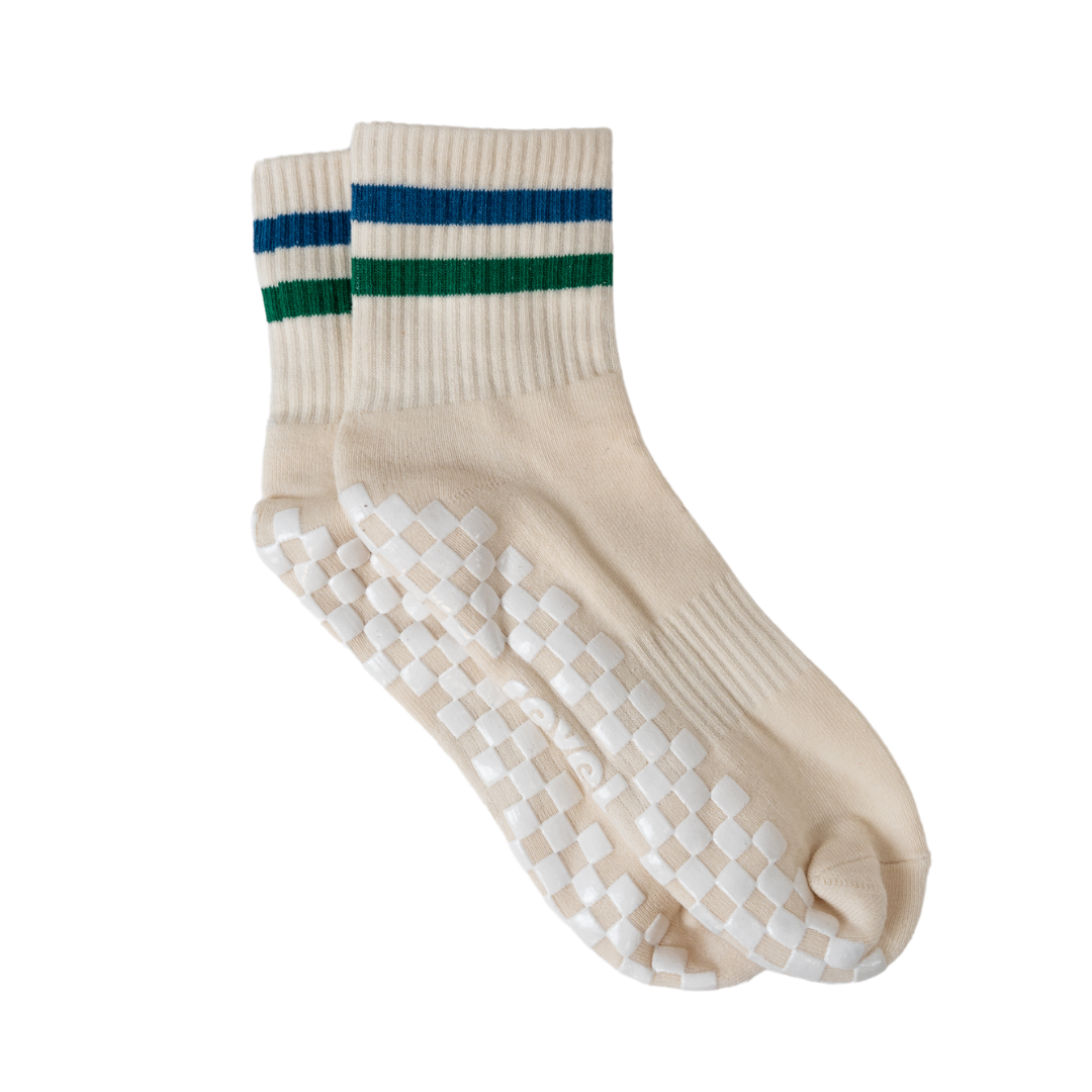 The Varsity Grip Sock by Revel: cream-colored socks with ribbed cuffs, blue and green top stripes, and a white checkerboard grip sole—ideal for Pilates or yoga. Set against a plain white background.