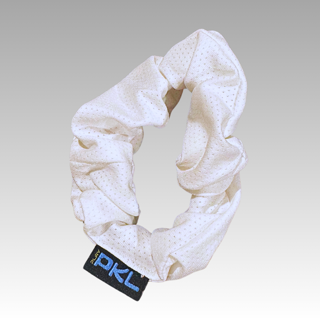 The Playly Store Shanti Pickleball Hair Scrunchie is white with a textured, perforated design. It features a black tag embroidered with blue and white PXL text, shown on a light gray gradient background.