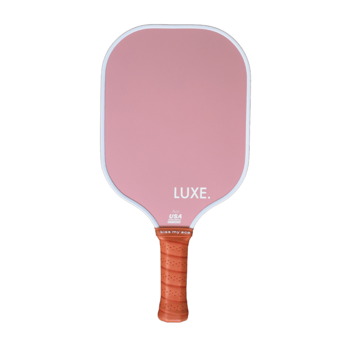 The Aesthetic Solids - Ace by LUXE Pickleball is a pink paddle with a light brown textured grip. It features "LUXE." in white, small text reading USA and "kiss my ace," and is USA Pickleball Approved. The background is white.