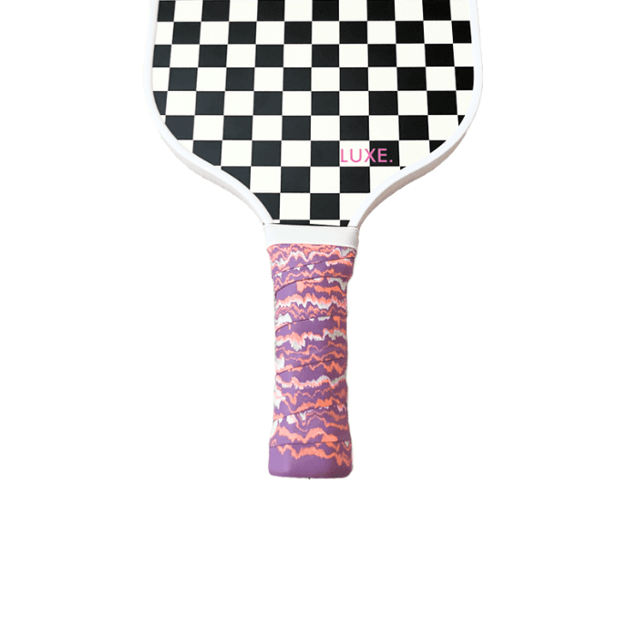 A LUXE Pickleball paddle featuring black-and-white checks, "LUXE." in pink by the handle, and a marbled overgrip in purple, pink, and orange—showcasing the Pickleball Paddle Grips on a plain white background.