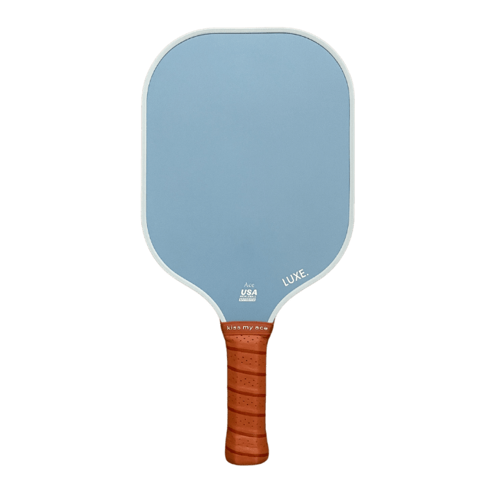 The Core Collection paddle by LUXE Pickleball features a light blue, textured carbon fiber surface, rounded corners, and a brown leather grip. "USA Pickleball Approved" and "LUXE." are printed near the handle and face on a white background.