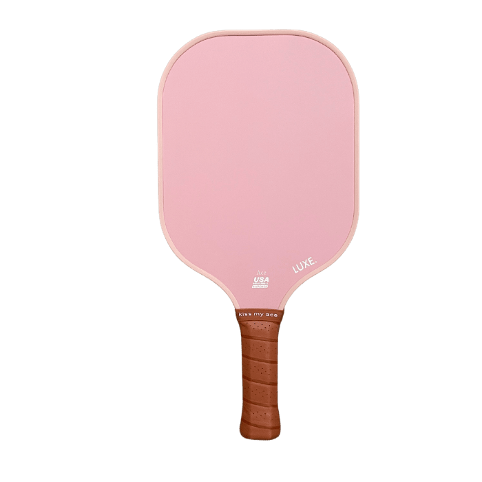 The LUXE Pickleball Core Collection paddle features a carbon fiber, pastel pink face with rounded rectangular edges, brown grip tape on the handle, "LUKE." in white, and a USA Pickleball Approved logo near the handle.