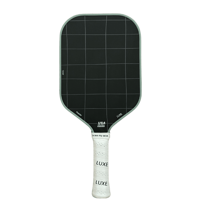 The LUXE Pickleball Premier paddle features a black, rectangular face with a white grid pattern made from raw Toray t700 carbon fiber. Its handle has white grip tape printed repeatedly with "LUXE" in black, all set against a plain white background.