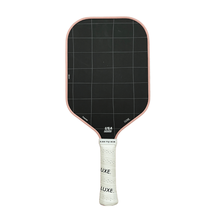 The LUXE Pickleball Premier paddle has a rectangular black face with a faint grid pattern, pink edge trim, and a white grip labeled LUXE. The face is made from premium Toray T700 carbon fiber. Shown against a plain white background.