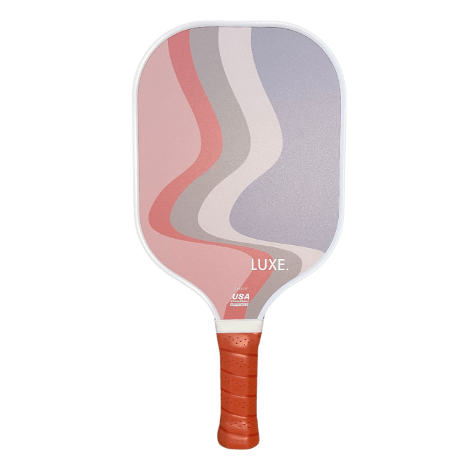 Introducing The Luka by LUXE Pickleball—a game paddle with a red, textured grip and a face featuring wavy pink, red, gray, and lavender stripes. Finished with "LUXE." and the USA Pickleball Approved logo for standout court style.