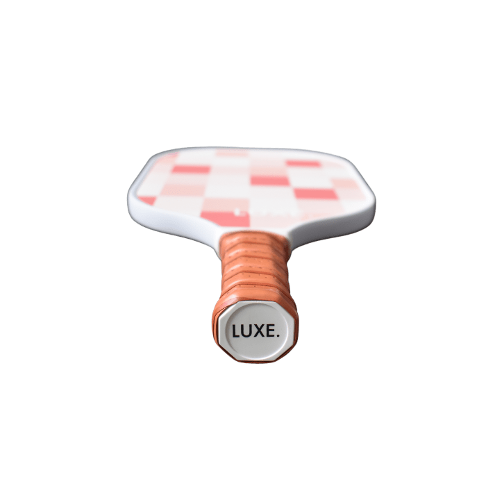 The LUXE Pickleball Checker paddle features a red and white checkered textured surface, a tan grip band on the handle, and an octagonal cap at the base with "LUXE" in bold black letters, all shown against a white background.