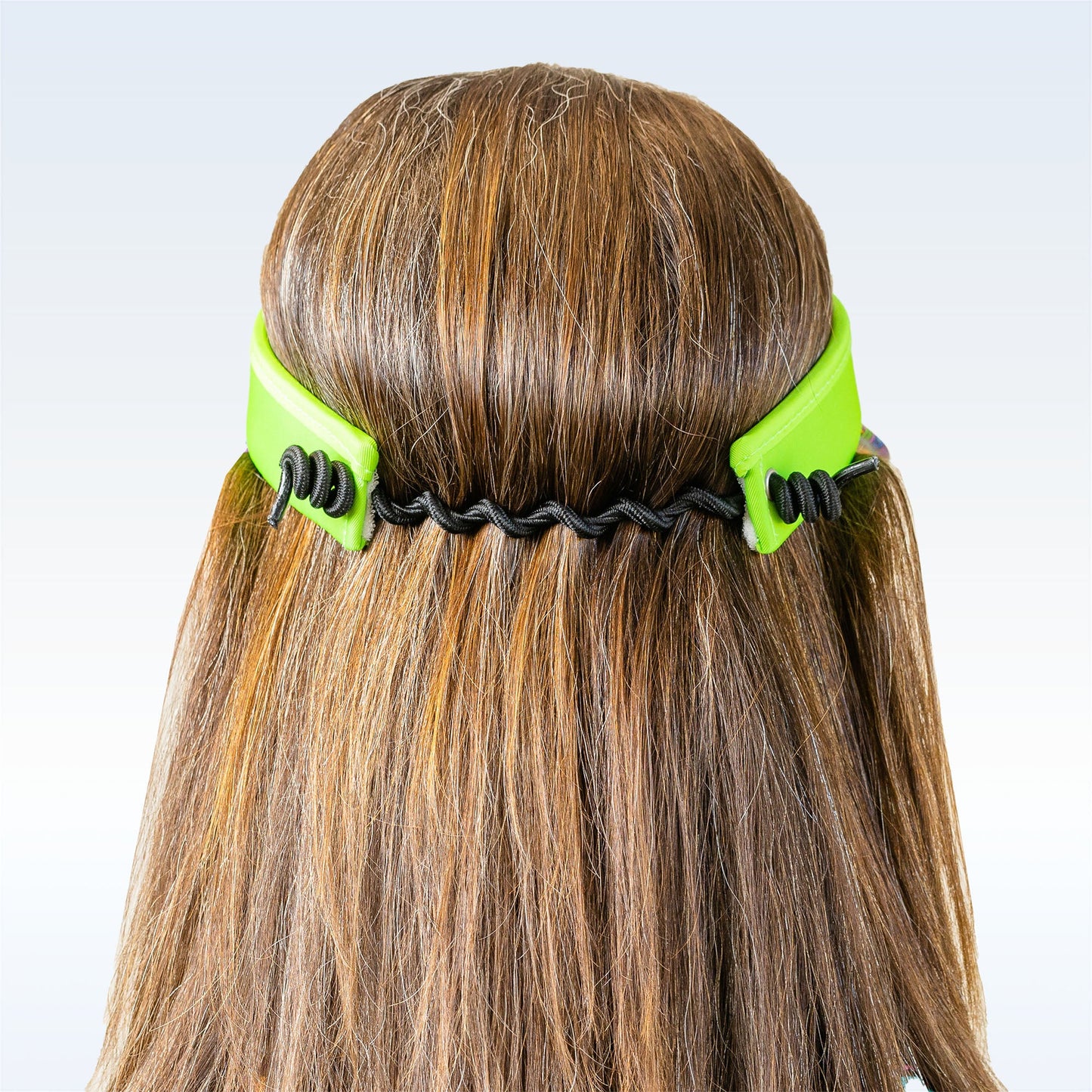 A person with long, light brown hair is seen from behind wearing the Pickleball Bella PB Visor Groovy, a black elastic band and bright green moisture-wicking headband positioned across the back of their head. The background is light and neutral.
