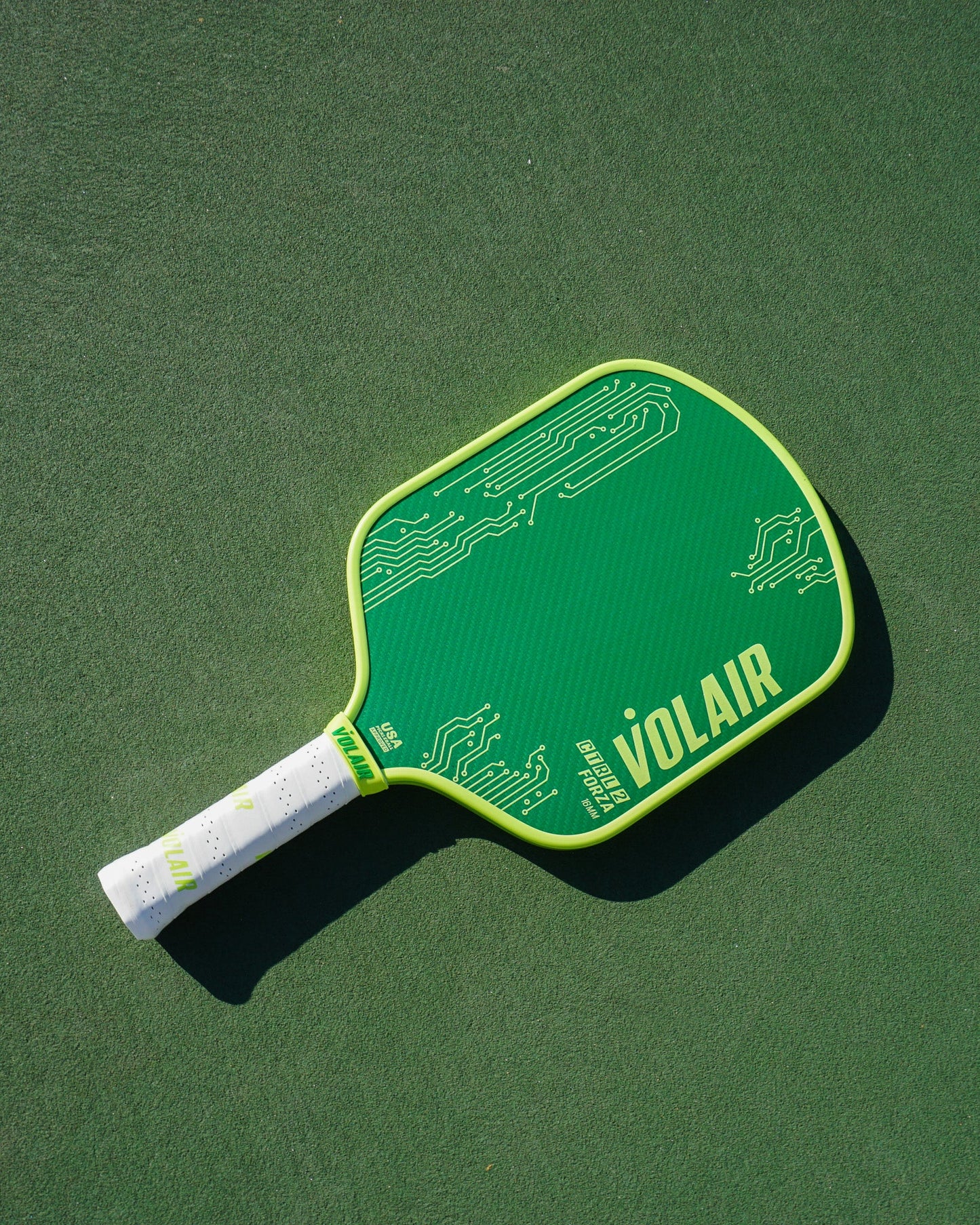 A Volair Pickleball CTRL 2 Forza 16mm green paddle with yellow edges, white grip, and circuit patterns (plus bold yellow “VOLAIR” and small text) rests on a green court.
