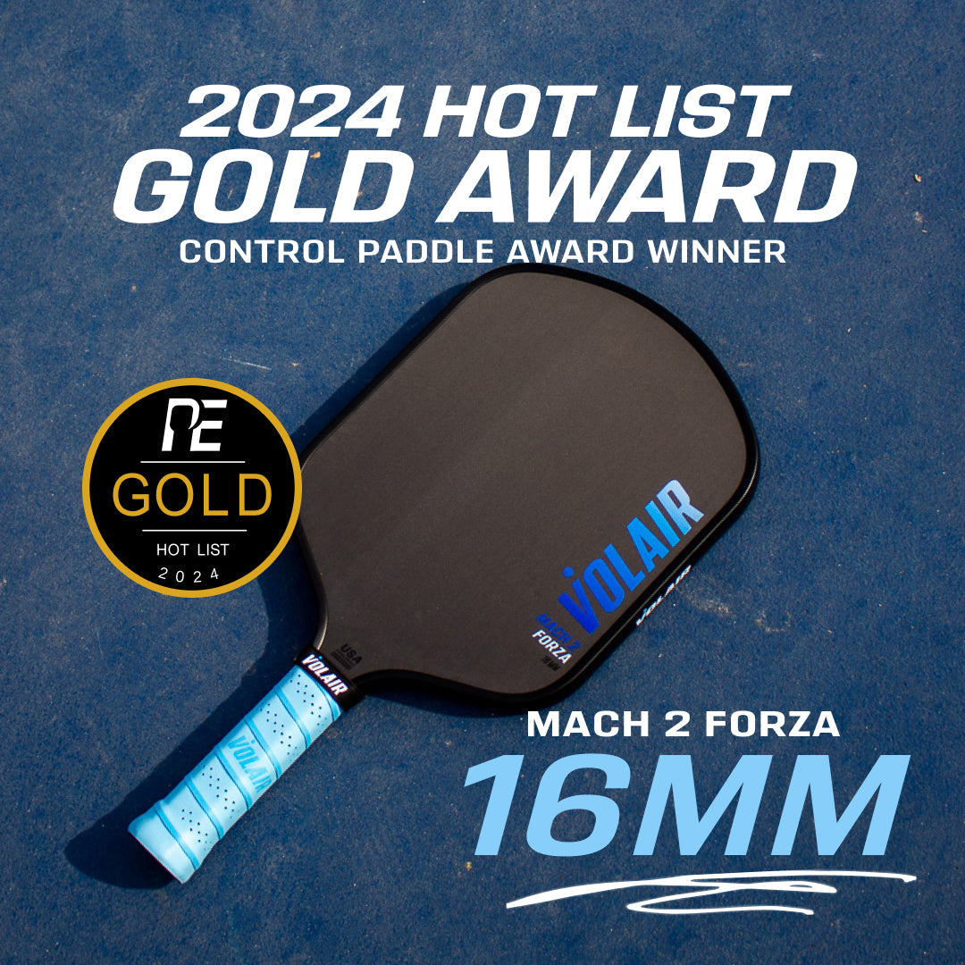 A black Volair Pickleball Mach 2 Forza Pickleball Paddle with a light blue grip lies on a blue court. USAP approved, it showcases a gold "2024 Hot List Gold Award, Control Paddle Winner, Mach 2 Forza 16mm" badge.