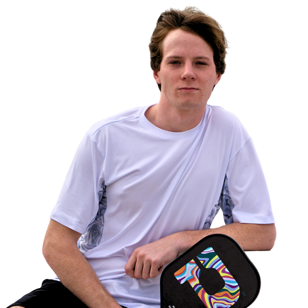 A young man with short brown hair wearing the Playly Store’s Playly - Warrior Tee 2.0 sits, resting his arm on a paddle with a colorful abstract swirl pattern against a plain white background.