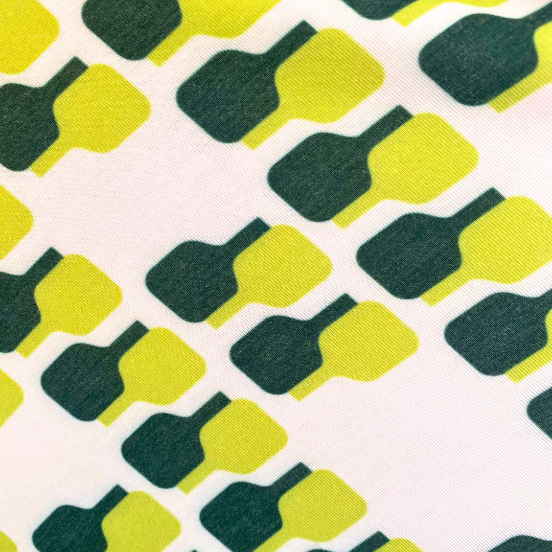 The Playly Store’s Warrior Tee 2.0 features bold green and yellow bottle shapes in diagonal rows on white, creating a geometric look ideal for pickleball or as a moisture-wicking performance shirt.