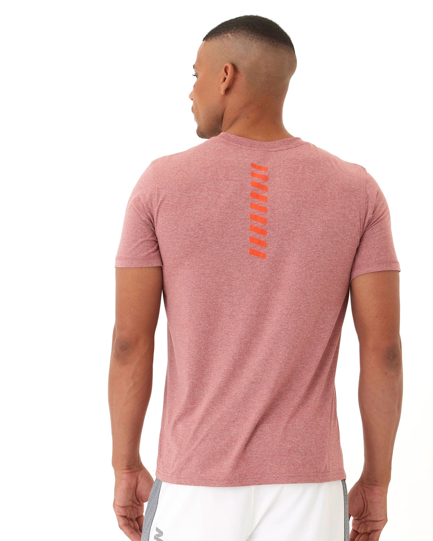 A man with short hair faces away, wearing the Wringer Wear Men's Short Sleeve Logo T-shirt in heathered red with orange vertical hash marks and a subtle logo on the upper back. He pairs it with white athletic shorts featuring a gray side stripe against a plain white background.