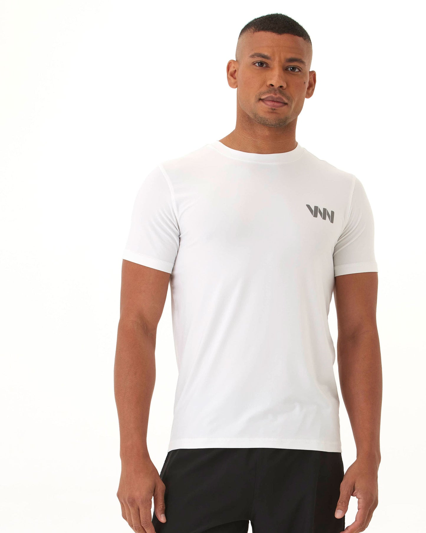 A man with short hair wears the Men's Short Sleeve Logo T-shirt by Wringer Wear, featuring a small logo on the left chest. He pairs it with black pants and stands against a light background, looking at the camera with a neutral expression.