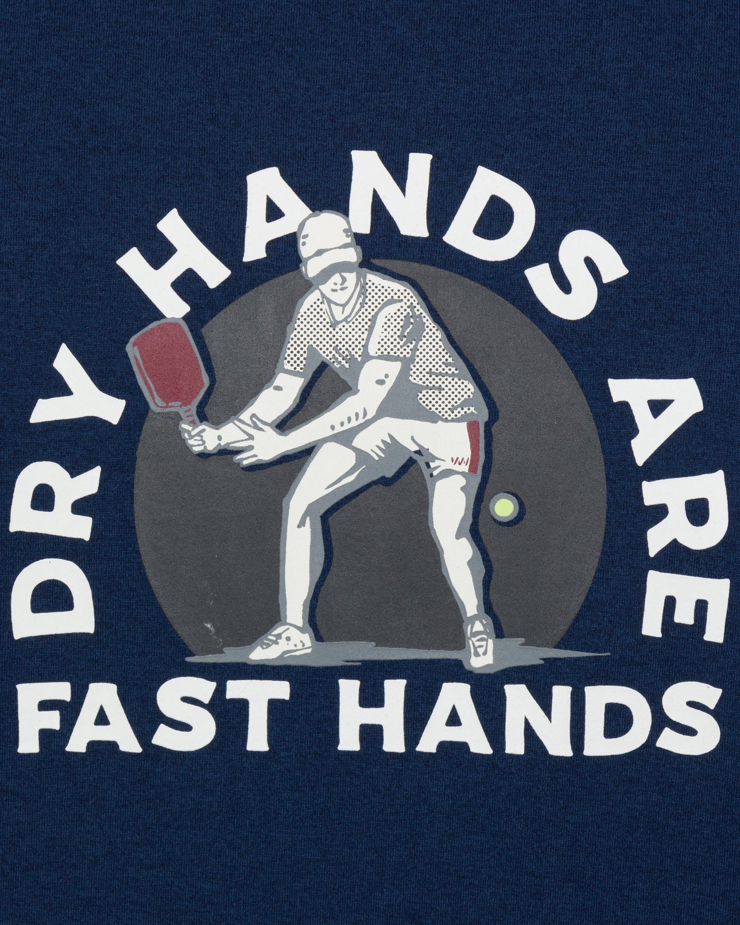 The Men's Short Sleeve Fast Hands Graphic T by Wringer Wear features an illustration of a pickleball player with "DRY HANDS ARE FAST HANDS" on a dark blue background—ideal for any performance-ready look.