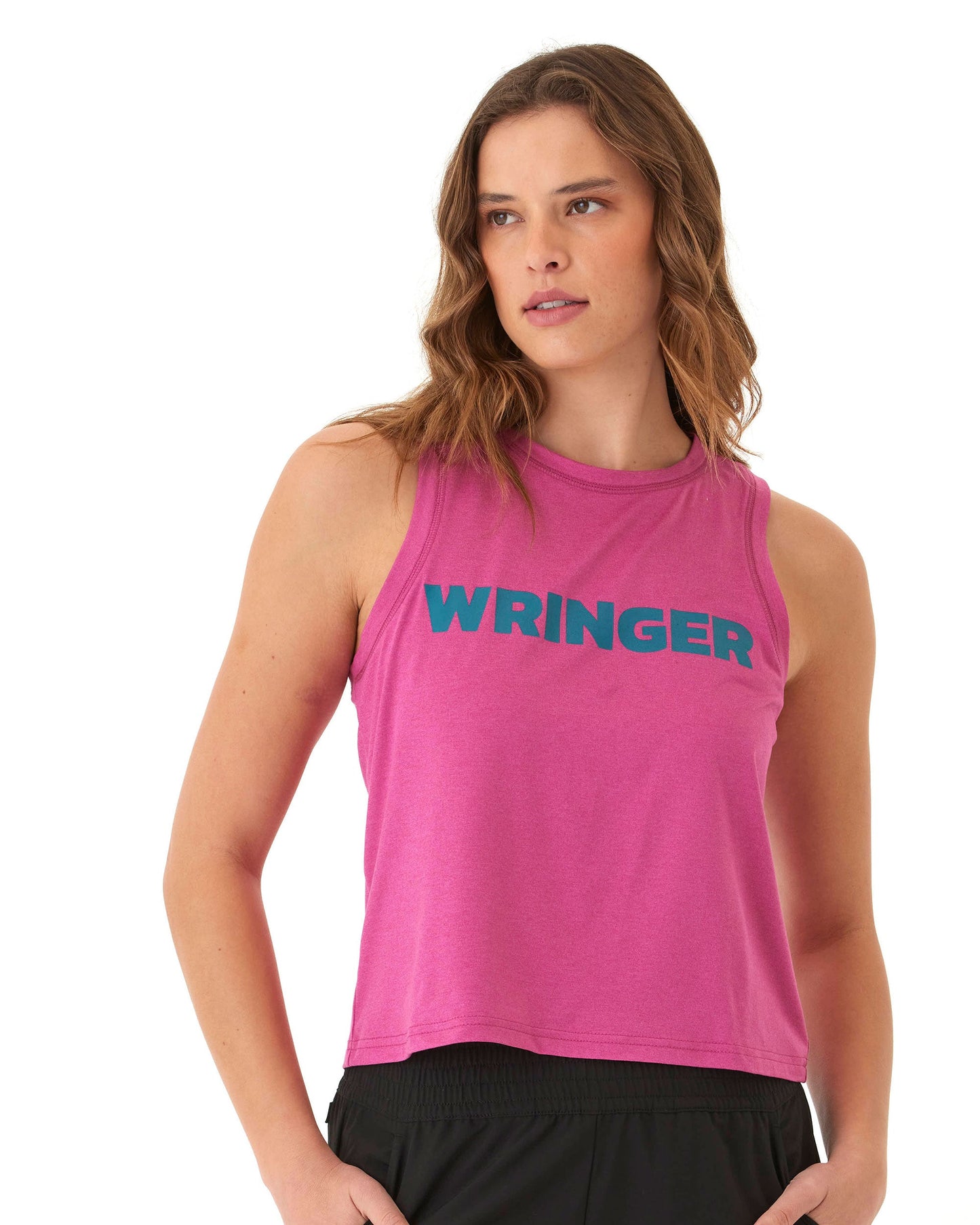 A woman with wavy brown hair wears the Wringer Wear Women's Performance Wringer Tank, a bright pink sleeveless crop top featuring bold blue "WRINGER" lettering, paired with black activewear bottoms against a plain white background.