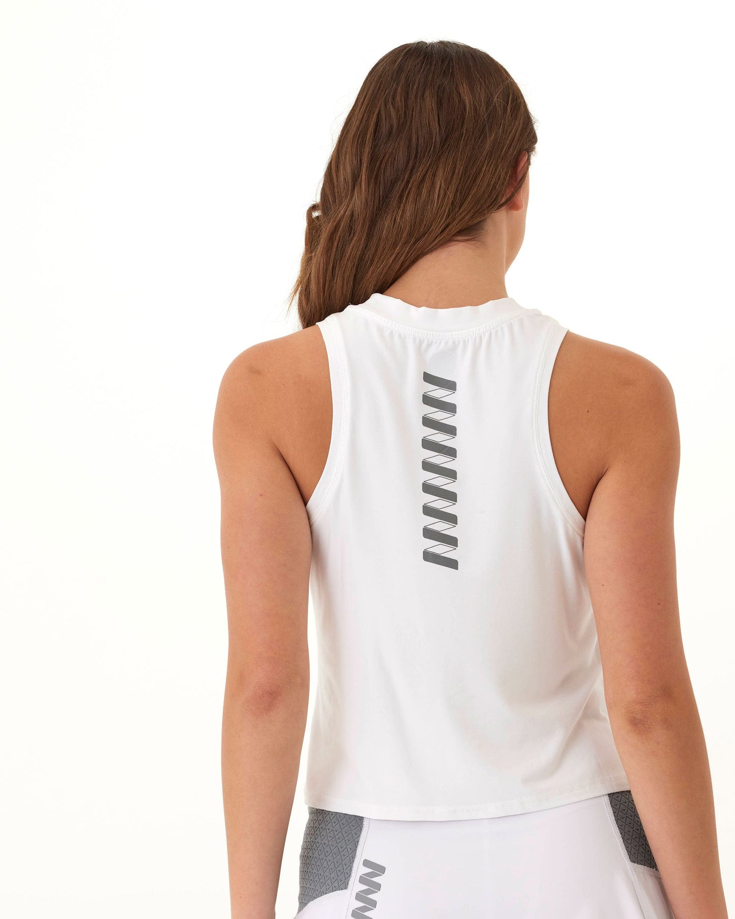 A woman with long brown hair faces away from the camera, wearing the Wringer Wear Women's Performance Wringer Tank with dark gray zigzag lines and a white skirt with gray accents, standing against a plain white background.