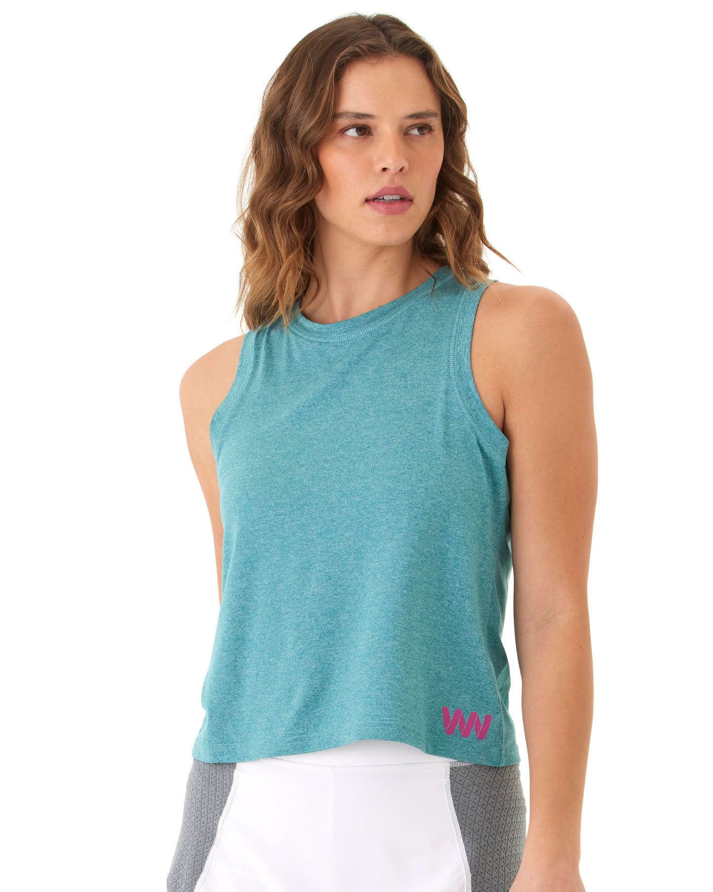 A woman with wavy, shoulder-length brown hair models the Wringer Wear Women's Performance Logo Tank in teal, featuring a small pink "WN" logo at the hem. She pairs it with white and gray shorts against a white background, looking slightly left.