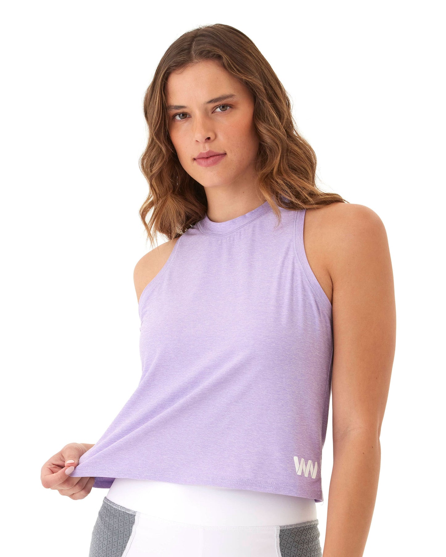 A woman with wavy brown hair models a sleeveless, light purple Wringer Wear Women's Performance Logo Tank and white high-waisted leggings, holding the hem out as she looks at the camera against a plain white background.