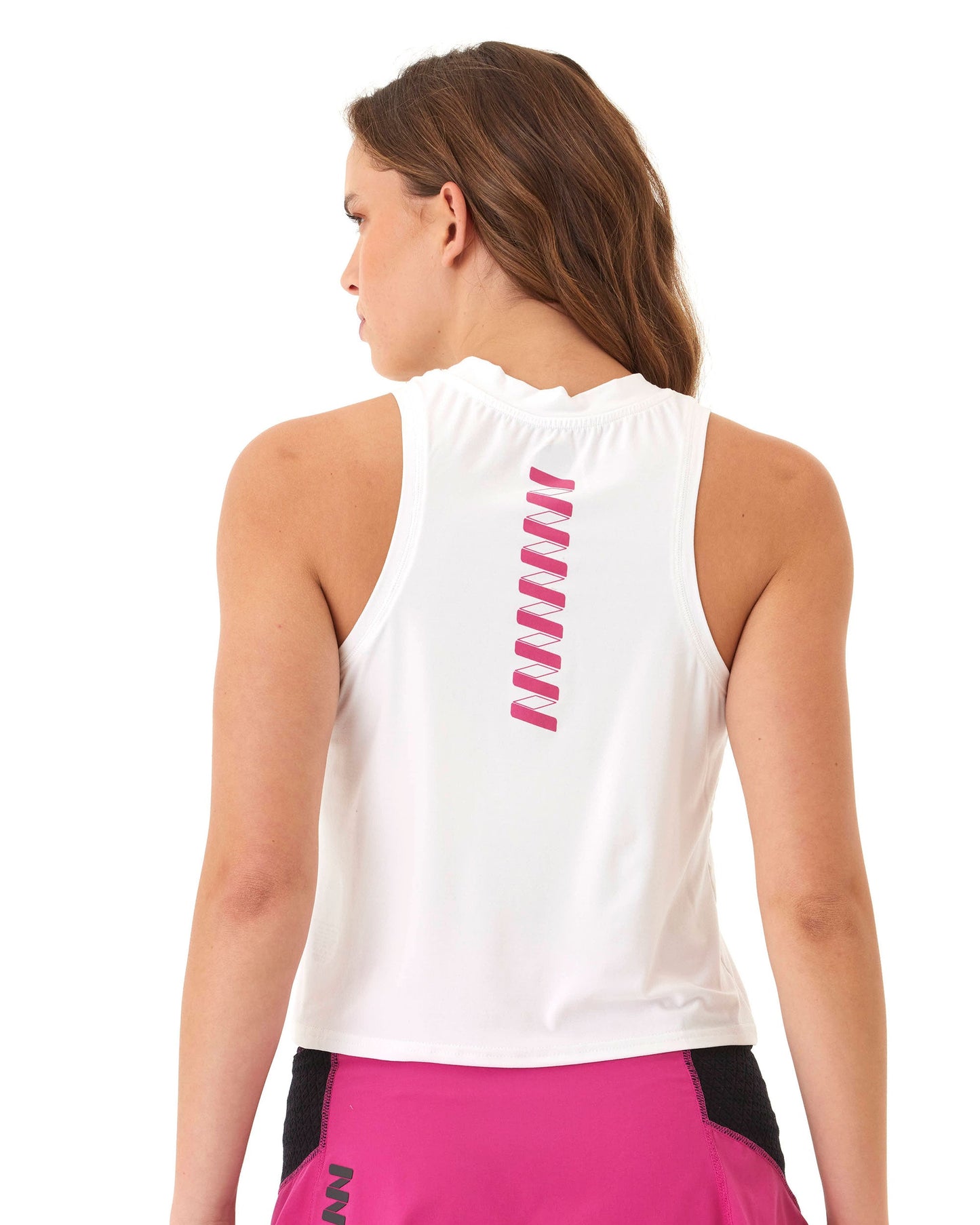 A woman with wavy brown hair wears the Wringer Wear Women's Performance Logo Tank, a breathable athletic top with a pink zigzag on the back, paired with pink shorts with black mesh, standing against a plain white background.