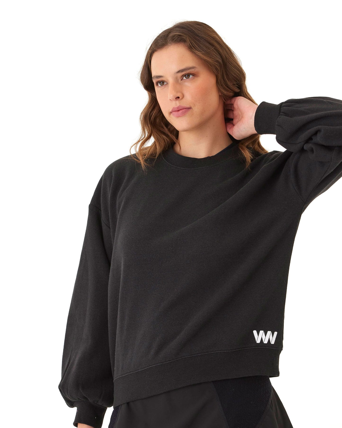A woman with wavy brown hair models the Wringer Wear Women's Crew Neck Sweatshirt. This loose black top features blouson sleeves and a small white WW logo near the hem, adding a stylish touch to her pickleball wardrobe.