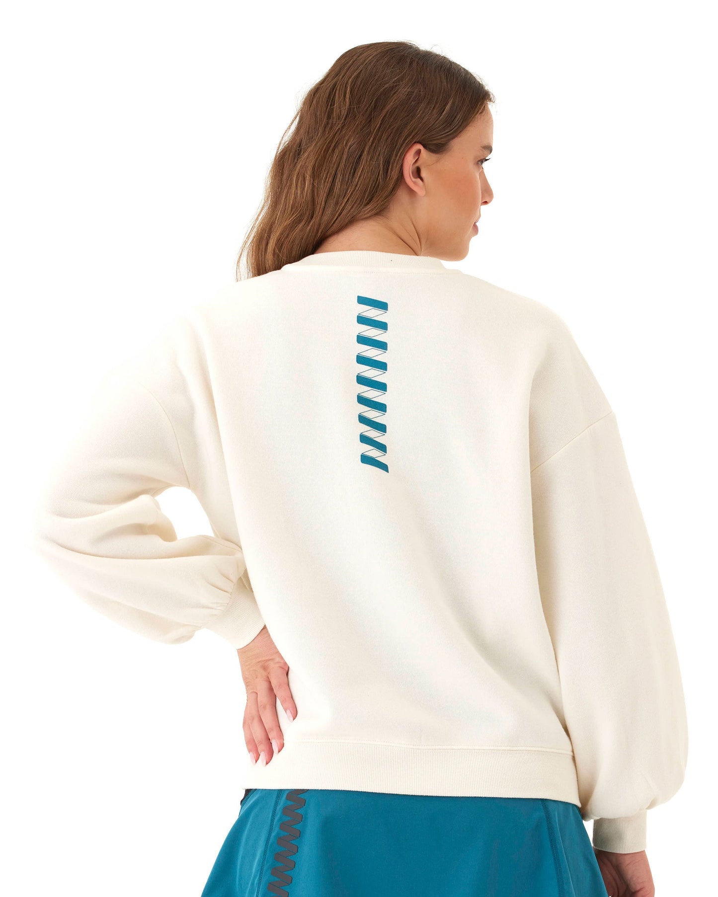 A woman with light brown hair models the Wringer Wear Women's Crew Neck Sweatshirt, featuring blouson sleeves and a vertical blue zigzag on the upper back, paired with a teal skirt against a plain white background.