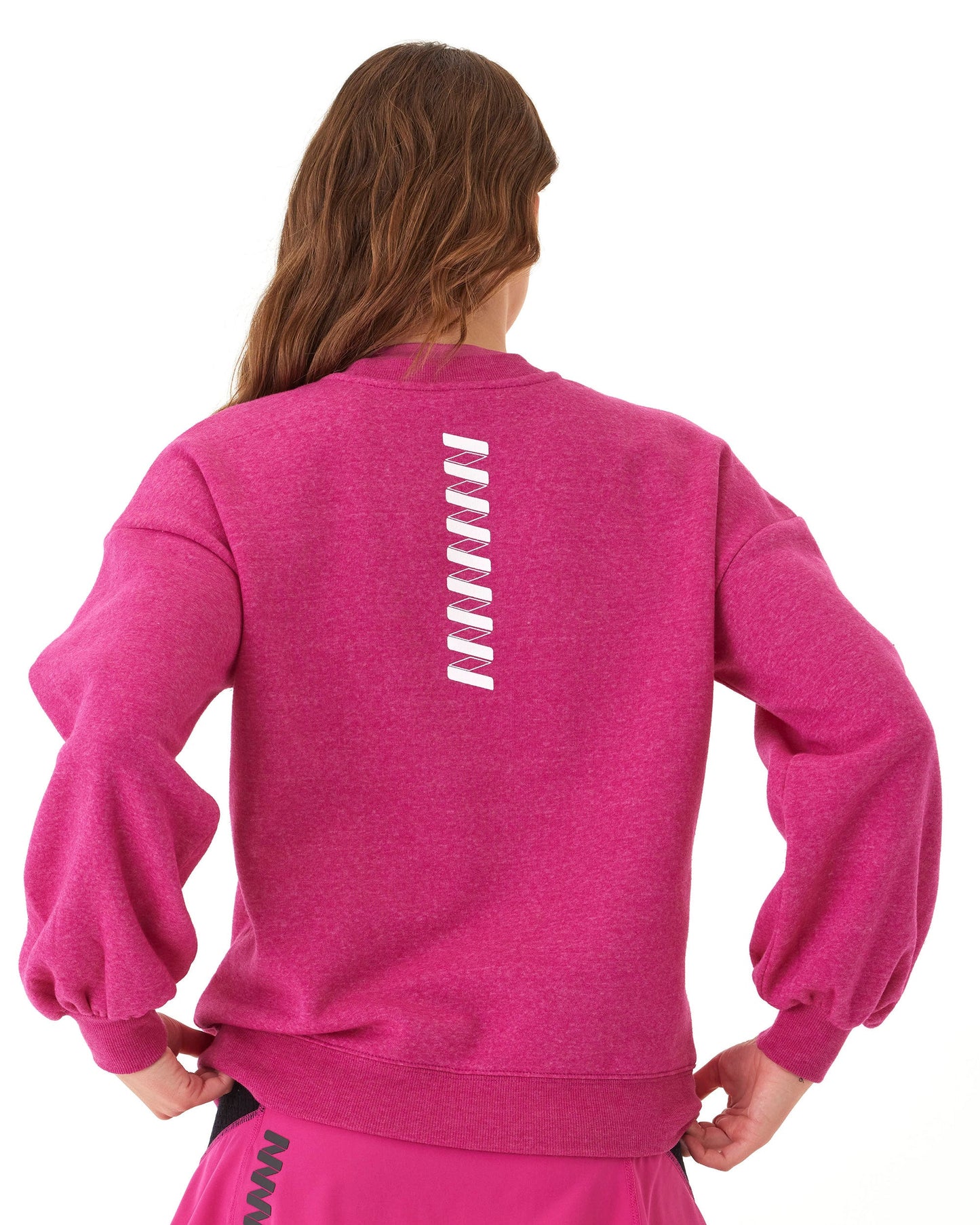 A woman with long brown hair, seen from behind, wears the Wringer Wear Women's Crew Neck Sweatshirt in bright pink with white zigzag lines down the back, paired with a matching skirt. The background is plain white.