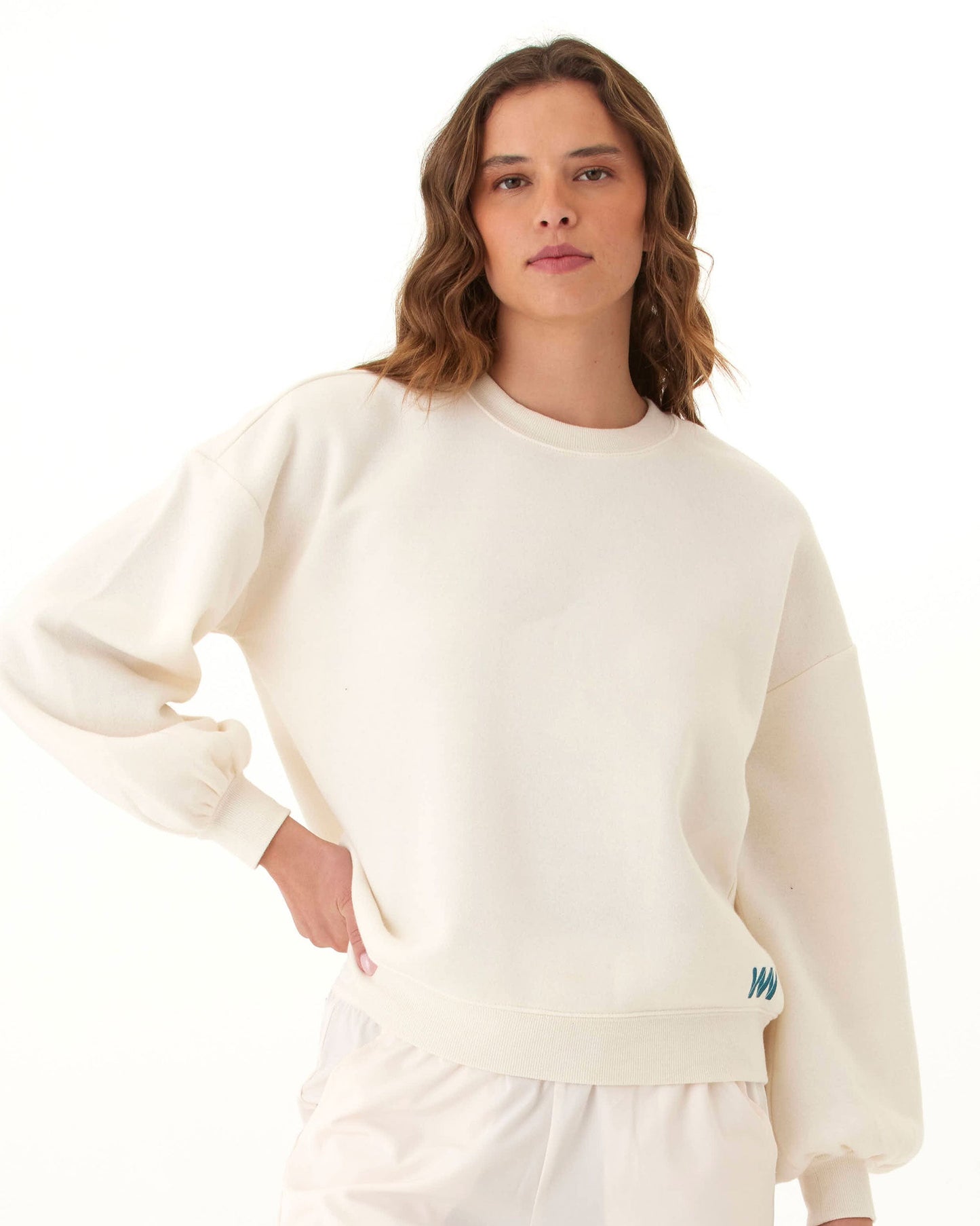 A woman with wavy brown hair models the Wringer Wear Women's Crew Neck Sweatshirt in off-white, pairing it with loose white pants for a confident, stylish look ideal for any pickleball wardrobe.