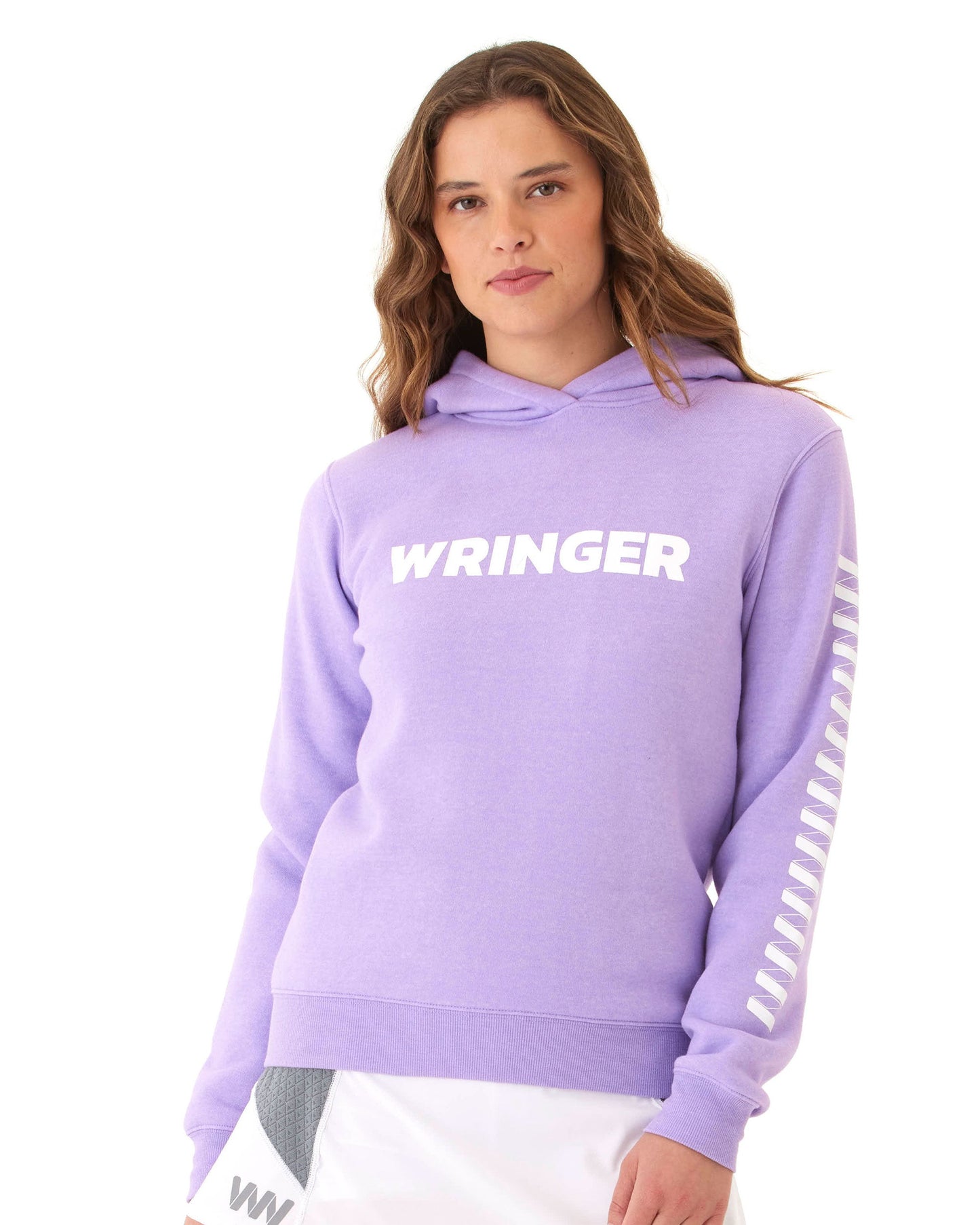A woman with wavy brown hair wears the Women's Core Wringer Graphic Hoodie by Wringer Wear in light purple, featuring bold white WRINGER lettering and a repeated “W” on the sleeve, paired with a white skirt with gray and black accents.