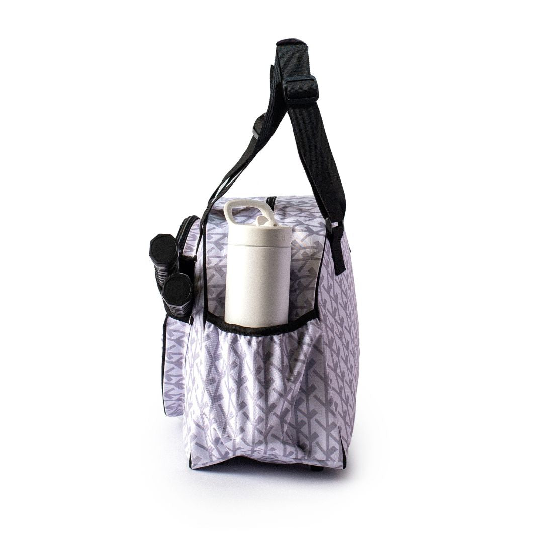 The Pik'le'Ball Sports Court Couture Premium Women's Pickleball Bag features a purple arrow pattern, black straps, multiple compartments, a paddle sleeve, and side pockets for essentials like a water bottle and accessories.