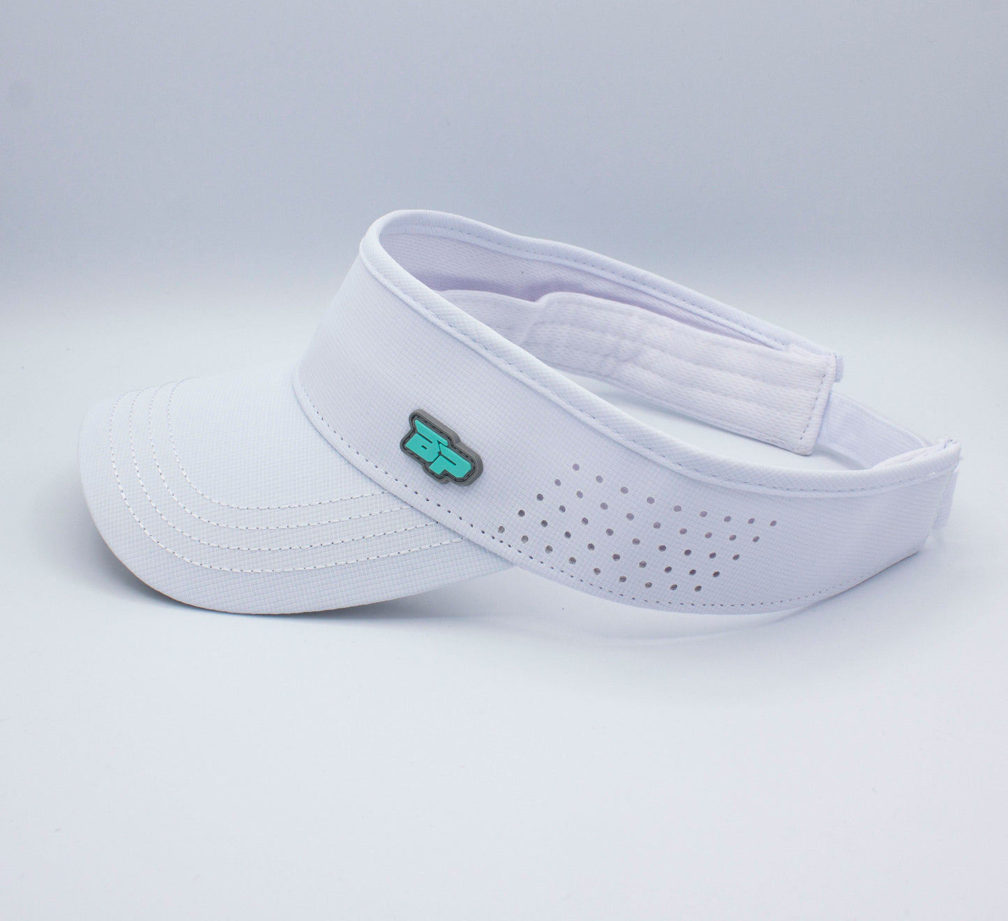 The Bodhi Performance ICON Visor is a white visor with a curved brim, small perforated holes for ventilation, an adjustable back strap, and a small teal and black front logo—ideal for staying cool on or off the pickleball court.